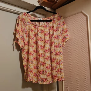 Blommig blus från Sincerely Led - Supersöt blommig blus från Sincerely Led i storlek L. Blusen har korta ärmar, rundad hals och ett luftigt fall. Färgerna går i gult, rosa och inslag av grönt och lila. Tillverkad i 100% viskos, perfekt för en fräsch och somrig look.