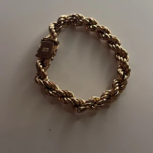 Guldigt tvinnat armband  - Snyggt armband i guldton med tvinnad kedja och rektangulärt lås där det står Armbandet har en chunky och glansig look som verkligen sticker ut. Perfekt för dig som gillar statement-smycken och vill ha något som syns.