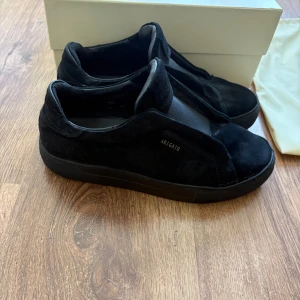 Axel Arigato clean 360 laceless  - Säljer ett par svarta sneakers från Axel Arigato i mocka med minimalistisk design och diskret logga i guld på sidan. Fins en minimal defekt se på bild 4 .Kommer även  med originalkartong och dustbag. Kan gå ner i pris vid snabb affär