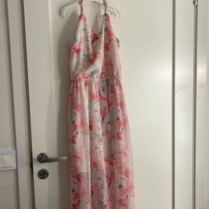 Blommig långklänning från Gina Tricot - Superfin långklänning från Gina Tricot med blommigt mönster i ljusa pastellfärger. Klänningen har smala axelband och en luftig passform, perfekt för varma dagar. Materialet känns lätt och flowy, vilket gör den extra bekväm.