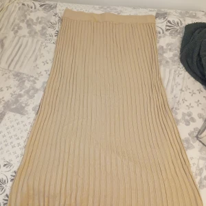 Beige ribbad långkjol från Gina Tricot - Säljer en beige ribbad långkjol från Gina Tricot. Kjolen är stickad med vertikala ränder och har en snygg slits baktill. Perfekt för dig som gillar en enkel men trendig look. Supermjuk och skön att bära hela dagen.