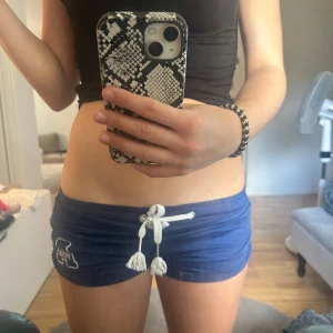 Blå 2000s mjukishorts - Säljer dessa sjukt snygga och bekväma shorts i storlek S. shortsen är marinblåa men vita snören och ett vitt a på vänstra sidan. Shortsen ger av sig en 2000a mini shorts vibe och man kan vika dem för att få dem mer lowrise än vad det är💕. 