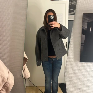 Grå kappa från 157 - Grå jacka från 157 i boxig modell med klassisk krage och stora knappar framtill. Jackan är i ullblandning och har två stora fickor framtill. Fodrad insida och extra knapp medföljer. Perfekt för lager-på-lager och snygg till jeans. Köpte förra hösten har knappt använt den ❤️ Köpte för 400kr 