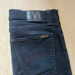 Svarta  jeans från Nudie Jeans - Svarta jeans från Nudie Jeans med klassisk femficksdesign och snygga svarta sömmar på bakfickorna. Modellen är skinny fit med normal midja och tillverkad i stretchig bomull. Perfekta för dig som gillar en smal siluett och stilren look.