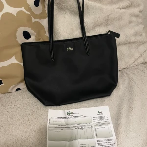 Lacoste concept handbag - A few times used city-/work bag. Durable material, resistant to scratches and rain. Material: synthetic material (textured).  Inside: - Spacious main compartment, suitable for A4 documents (just and just) - Key holder / lanyard - One zipper compartment   Dimensions: 35cm x 25cm x 14cm 