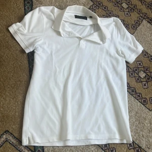 Vit pikétröja Lyle & Scott, storlek L - Vit pikétröja från Lyle & Scott i storlek L. Klassisk design med korta ärmar, krage och knappslå. Tröjan har det ikoniska broderade Lyle & Scott-märket i gult på bröstet. Tillverkad i mjuk bomull som är skön mot huden. Har små fläckar som kan gå bort med en tvätt