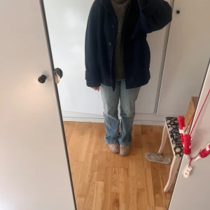 Mörkblå ullkappa med huva - Säljer en mörkblå kappa i ull med stor huva och knappar framtill. Jackan har en loose passform, stora fickor och breda ärmslut. Perfekt för dig som gillar en chill och stilren look under höst och vinter.