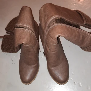 Bruna stövlar med kilklack - Snygga bruna stövlar i syntetmaterial med kilklack och dragkedja på sidan. Perfekta för höst och vinter med en stilren design. Dom är i jättebra skick och knappt använda.