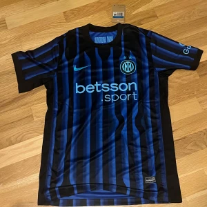 Inter Milan 25/26 Hemmaställ - Inter Milan hemma ställ 25/26 från Nike med klassiska svarta och blå vertikala ränder. Tröjan har korta ärmar, klubbmärke och sponsorer tryckta på bröstet och ärmen. Tillverkad i lätt och ventilerande polyester.