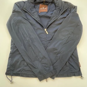 Mörkblå vindjacka från Moncler - Snygg mörkblå vindjacka från Moncler med broderad logga på ryggen.  Mått kan fixas vid köp.