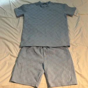 Blå shorts från Gucci med GG-mönster - Snygga ljusblå shorts från Gucci med det klassiska GG-mönstret över hela tyget. De har snörning i midjan och en bakficka. Materialet känns mjukt och lyxigt, perfekt för dig som vill ha en clean och exklusiv look i sommar.