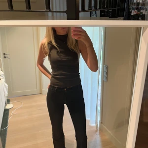 Svart ärmlös halvpolo topp - Säljer en brun ärmlös polotopp med tight passform. Toppen har medelhög krage och är i ett stretchigt material som sitter snyggt mot kroppen. Perfekt att styla med jeans eller kjol för en clean look. Aldrig använd