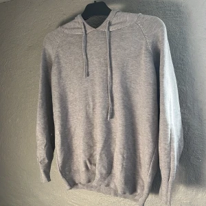 Grå stickad hoodie med huva - Mjuk och stilren grå hoodie med huva och snörning. Tröjan är stickad och har långa ärmar samt ribbade muddar vid ärmslut och nederkant. Inte använd någon gång och helt ny. Stryker och fixar den innan köp och leverans! Fråga gärna frågor om tröjan eller skicka prisförslag och diskutera pris! Tar gärna emot frågor.