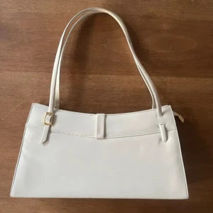 Gräddvit elegant handväska  - Elegant Vit Handväska - 99 kr!  Uppgradera din stil med denna vackra vita handväska! Denna väska är perfekt för alla tillfällen, från jobbet till en kväll ute. Dess stilrena design och kvalitativa utförande ger en sofistikerad look. Köp den nu för endast 99 kronor och lägg till en touch av elegans till din garderob! Missa inte chansen att äga denna tidlösa accessoar.