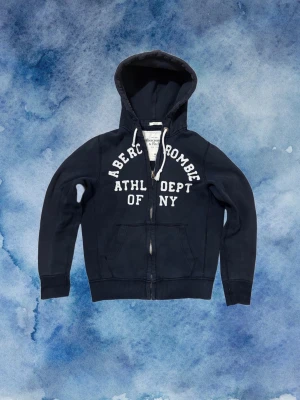 Vintage Abercrombie & Fitch Zip Hoodie - Säljer denna as feta Abercrombie & Fitch Zip Hoodien | Mycket bra skick förutom ett litet hål under ”Aberc” - se bild 4, men syns knappast då tröjan ska ha en sliten design | Storlek M, Längd ≈ 67cm, Bredd armhåla - armhåla ≈55cm | Modell 175cm, 68kg | Hör av vid funderingar! Pris kan diskuteras!