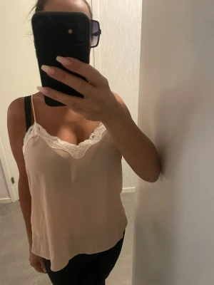 linnetopp med spetskant - Säljer ett linne med spetskunskapen  med tunna axelband och v-ringning dekorerad med vit spets. Toppen har en lös passform och är tillverkad i ett mjukt, lätt material som ger en skön känsla. Perfekt för varma dagar eller att styla lager på lager. Oversize modell så passar de flesta då den är större i strk