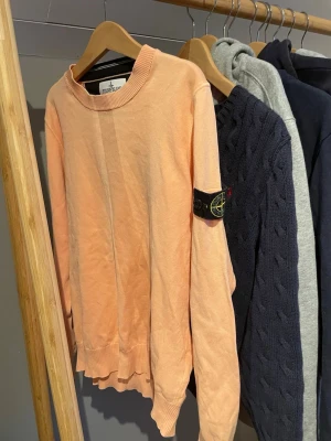 Persikofärgad tröja från Stone Island - Säljer en persikofärgad långärmad tröja från Stone Island Junior. Tröjan har rund hals, ribbade muddar och den klassiska loggan på vänster ärm. Tillverkad i mjuk bomull, perfekt för dig som vill ha en clean och stilren look. Slå bara en pling 🛎️ kring några funderingar. 