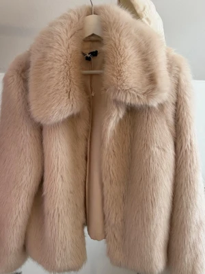 Beige pälsjacka med stor krage - Supermjuk och fluffig beige pälsjacka med bred krage och rak passform. Jackan har en klassisk look och är fodrad på insidan. Perfekt för dig som vill ha en mysig och trendig jacka med lite lyxig känsla. Priset kan diskuteras.