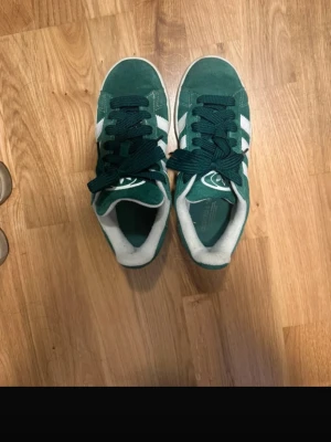 Gröna Adidas Gazelle sneakers mocka - Säljer ett par gröna Adidas Gazelle sneakers i mocka med klassiska vita ränder på sidorna och vit sula. De är använda, men i bra skick! Perfekta för dig som gillar retrostil och streetwear.