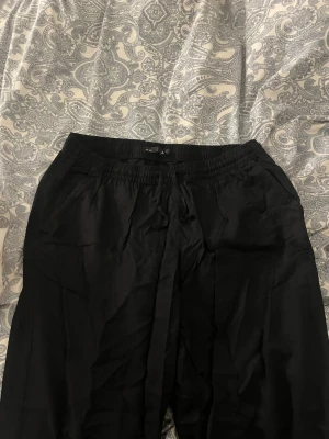 Svarta linnebyxor med snörning - Säljer ett par svarta linnebyxor med resår i midjan och snörning framtill. Byxorna har raka ben och sidofickor, perfekta för en chill och avslappnad stil. Materialet är lätt och luftigt, vilket gör dem sköna att bära under varmare dagar.