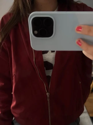 Vinröd bomberjacka från Monki - Säljer en vinröd bomberjacka från Monki i storlek M. Jackan har dragkedja framtill, ribbade muddar och två fickor på sidorna. Materialet känns mjukt och lätt, perfekt för lager på lager. Enkel och stilren design som passar till det mesta.