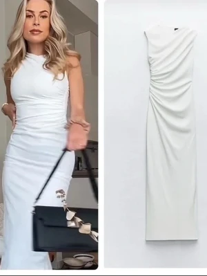 Vit långklänning med drapering - Säljer en elegant vit långklänning med draperad detalj på sidan. Klänningen är ärmlös och har en figurnära passform som framhäver siluetten. Perfekt för dig som vill ha en stilren och modern look.