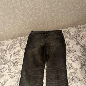Svarta slim jeans med slitningar - Säljer ett par svarta jeans med snygga slitningar och tvättade detaljer. Jeansen har fem fickor, knappgylf och smal passform som sitter tajt längs benen. Perfekta för dig som gillar en modern och clean look.