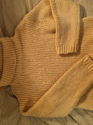 Beige stickad polotröja med guldtråd - Säljer en chunky beige stickad polotröja med ribbade muddar och detaljer av guldtråd i halsen. Tröjan har lång ärm och hög polokrage, perfekt för kalla dagar. Den grova stickningen ger en mysig och trendig look.