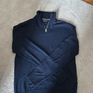 Marinblå half zip tröja Jack & Jones - Snygg marinblå långärmad tröja från Jack & Jones med half zip-dragkedja och hög krage. Tröjan är stickad i mjukt material och har ribbade muddar vid ärmslut och nederkant. Storlek xs men sitter mer som S