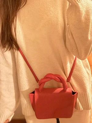 Rosa atp väska  - Säljer en snygg rosa axelväska med twistat handtag och lång axelrem. Väskan har en stilren, boxig form och stängs med magnetknapp. Perfekt storlek för det viktigaste och ger en cool touch till din outfit. 