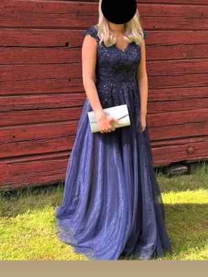 Marinblå balklänning med spets och glitter - Säljer en marinblå balklänning från JJ’s house som endast är använd en gång. V-ringning fram och bak, spetsdetaljer och glittrig ovandel. Lite för lång för mig som är 162. Insydda ilägg vid bröstet. Perfekt för bal eller student!