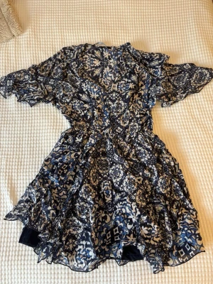 Blommig kortklänning från Zara - Säljer en luftig kortklänning från Zara med blommigt mönster i marinblått, vitt och ljusblått. Klänningen har volangdetaljer, v-ringning och korta ärmar. Perfekt för sommarens alla tillfällen!