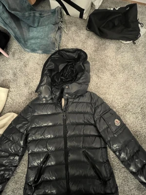Marinblå Moncler pufferjacka med huva - Säljer en svart pufferjacka från Moncler med huva och dragkedja framtill. Jackan har två snedställda fickor med dragkedja och Moncler-logga på ärmen. Perfekt för kalla dagar och riktigt snygg till jeans eller mjukis. Äkthetsbevis på bild 2❤️Andvänd endast en vinter därav näst intill helt ny! O därför priset