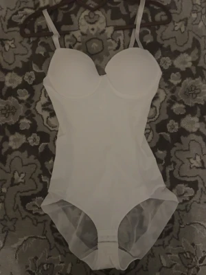 Vit bodysuit med meshdetaljer - Jätte fin figursydd body. snyggt att ha till fina tillfällen/utgångar. classy och fin. Har bara testat på den så den är aldrig använd. Den är S men kan även passa XS för den formar kroppen 