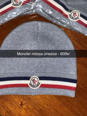 Grå Moncler mössa med ränder - Snygg grå mössa från Moncler med klassiska ränder i marinblått, vitt och rött längst ner samt Moncler-logga framtill. Mössan är ribbstickad och har en clean look som passar till allt. Tillverkad i Italien och känns riktigt lyxig.