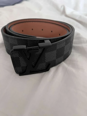 L-bälte  - Snyggt L-bälte i Damier-mönster med svart spänne.  Storlek: 110 cm