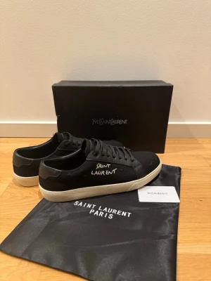 Svarta Saint Laurent sneakers med vit sula - Svarta sneakers från Saint Laurent med vit sula och handskriven logga på sidan. Skorna har ovandel i canvas och detaljer i skinn, samt klassisk snörning. Perfekta för dig som gillar stilrena och exklusiva sneakers med en unik touch. Aldrig använda. PRISET KAN DISKUTERAS VID SNABB AFFÄR!