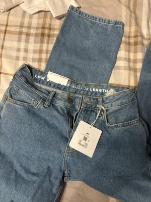 Ljusblå low waist jeans med raka ben - Säljer ett par ljusblå jeans från Monki med low waist och raka ben. Klassisk femficksmodell med knapp och dragkedja framtill. Jeansen är i mjukt bomullsmaterial och har en avslappnad passform. Perfekta för en chill och trendig look.