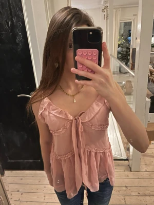 Rosa volangig linnetopp med knyt - Säljer en superfin ljusrosa linnetopp med volangdetaljer och knyt framtill. Toppen har tunna axelband och är tillverkad i ett lätt, luftigt material som passar perfekt till sommaren. 