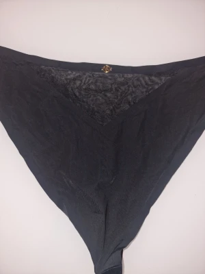 Svart Victoria's Secret trosa - Svart Victoria's Secret braziliantrosa med triangelformad meshdetalj framtill och en liten guldfärgad VS-logga i midjan. Trosan har en clean look och är tillverkad i mjukt, stretchigt material för skön passform. Ny givetvis.