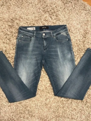 Replay Hyperflex ljusblå jeans - Snygga Replay Hyperflex jeans i klassisk blå tvätt med lätt slitning. Modellen har fem fickor, normal passform och midwaist. Jeansen är tillverkade i stretchigt denim för extra komfort och rörelsefrihet. Perfekta för dig som gillar en stilren och bekväm look.