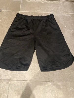 Svarta träningsshorts från H&M Move - Säljer ett par svarta träningsshorts från H&M Move. De är tillverkade i ett lätt och ventilerande meshmaterial med elastisk midja. Perfekta för gymmet eller löprundan och har en loose fit för maximal rörelsefrihet.