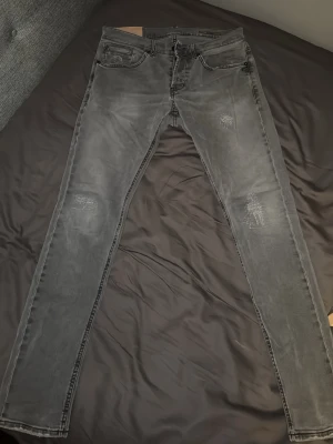 Grå Dondup Jeans - Säljer ett par grå Dondup jeans med slitna detaljer på både fram- och bakfickor samt knän. Jeansen har fem fickor, normal midja och är tillverkade i stretchig denim för en tight passform. Perfekta för dig som gillar en avslappnad men trendig stil.