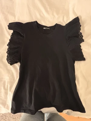 Svart topp med spetsärmar från Zara - Supersnygg svart topp från Zara med breda, volangiga spetsärmar. Tröjan är knappt ändvänd. Skriv för fler bilder eller om ni skulle vilja pruta.