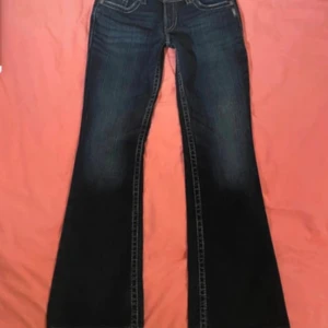 Low rise Bootcut jeans från Silver  - Lågmidjade bootcut jeans från Silver Jeans Co med snygga kontrastsömmar och klassisk femficksdesign. Jeansen har låg midja och är tillverkade i slitstarkt denim med lätt tvättad look. Perfekta för dig som gillar en avslappnad men ändå trendig stil.