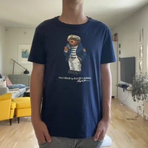 Mörkblå Polo Bear t-shirt Ralph Lauren - Snygg mörkblå t-shirt från Ralph Lauren med Polo Bear-tryck på bröstet. Slim fit-modell med rund hals och korta ärmar. Materialet är mjuk bomull som känns skönt mot huden. Perfekt för dig som gillar klassisk stil med en twist. Large men liten i storleken! Modellen på bilden är 176 cm!
