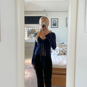 Mörkblå omlottopp med knyt - Snygg mörkblå omlottopp med långa ärmar och djup v-ringning. Toppen har en croppad passform och knyts framtill med långa band. Perfekt för dig som gillar trendiga och stilrena plagg med en twist.