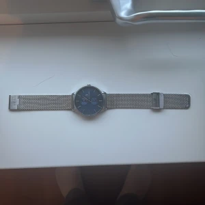 Silverfärgad klocka Black Oak Sweden - Stilren klocka från Black Oak Sweden med blå urtavla och två mindre subdials. Armbandet är i silverfärgat metallnät som ger en modern vibe. Rund boett i blankt stål och minimalistiska index. Perfekt för dig som gillar cleana accessoarer.