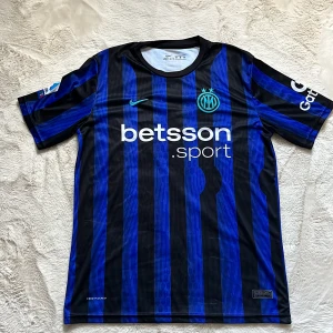 Inter Milan Lautaro 10 Nike fotbollströja - Snygg Inter Milan matchtröja med blå och svarta ränder, Nike Dri-Fit material och tryckta sponsorer. På ryggen står Lautaro och nummer 10 i vitt. Broderat klubbmärke med två stjärnor på bröstet och Serie A-märke på ärmen. Perfekt för dig som älskar fotboll och vill ha en äkta supportertröja.