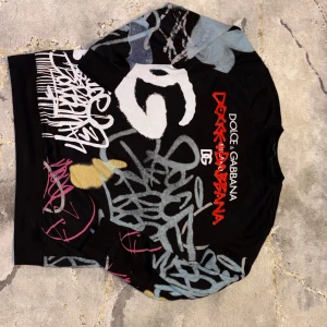 Dolce Gabbana Graffiti Tröja - Snygg svart tröja från Dolce & Gabbana med unikt graffitiinspirerat tryck i vitt, blått, rött, gult och rosa. Långärmad modell med rund hals och coola street-vibes. Perfekt för dig som vill sticka ut med en statement piece.